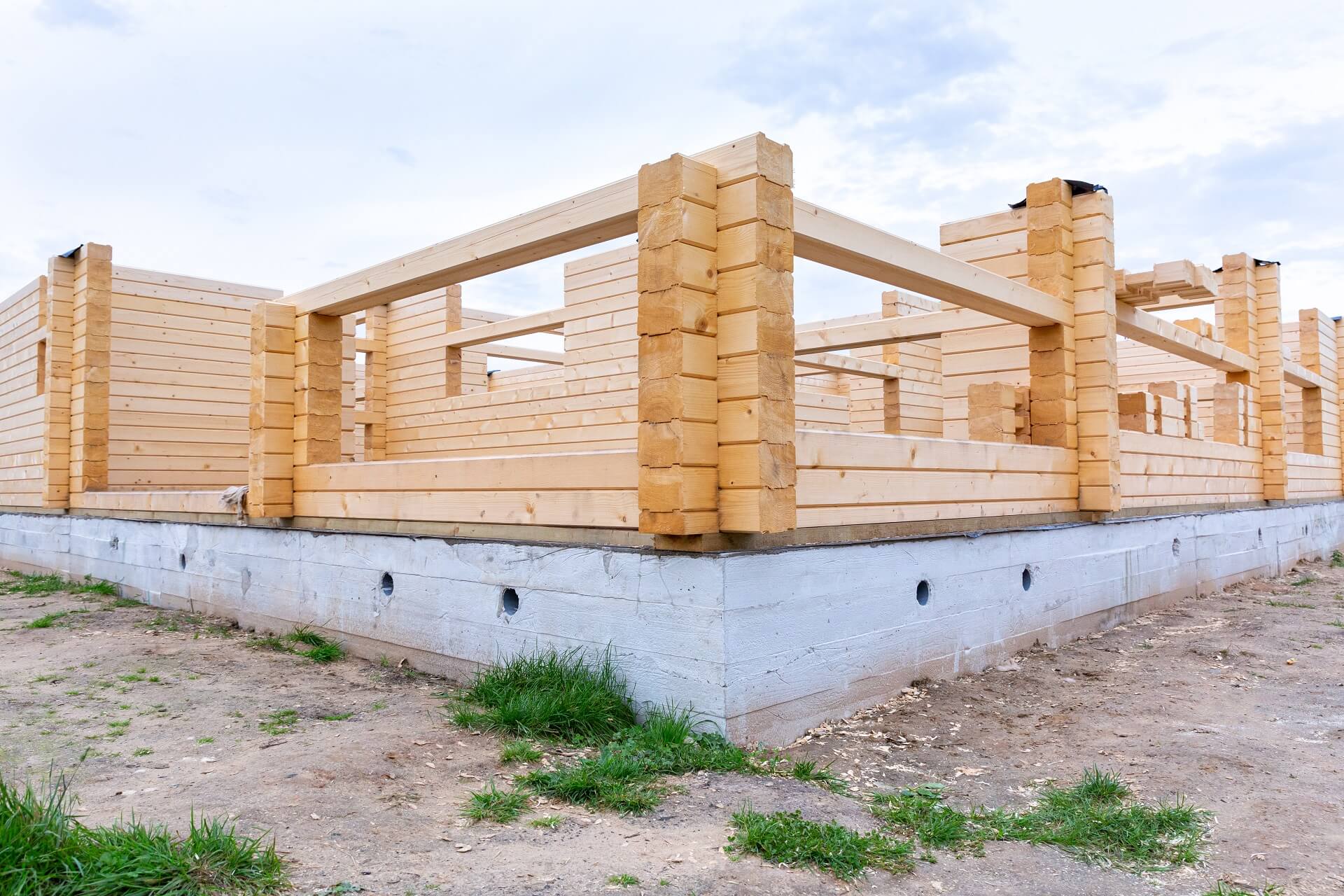 Ein Bild, das den Bauprozess eines Holzhauses auf einem Zementfundament zeigt. Erfahren Sie mehr über die Bedeutung von Stabilität und einer soliden Grundlage in diesem Bauprojekt.