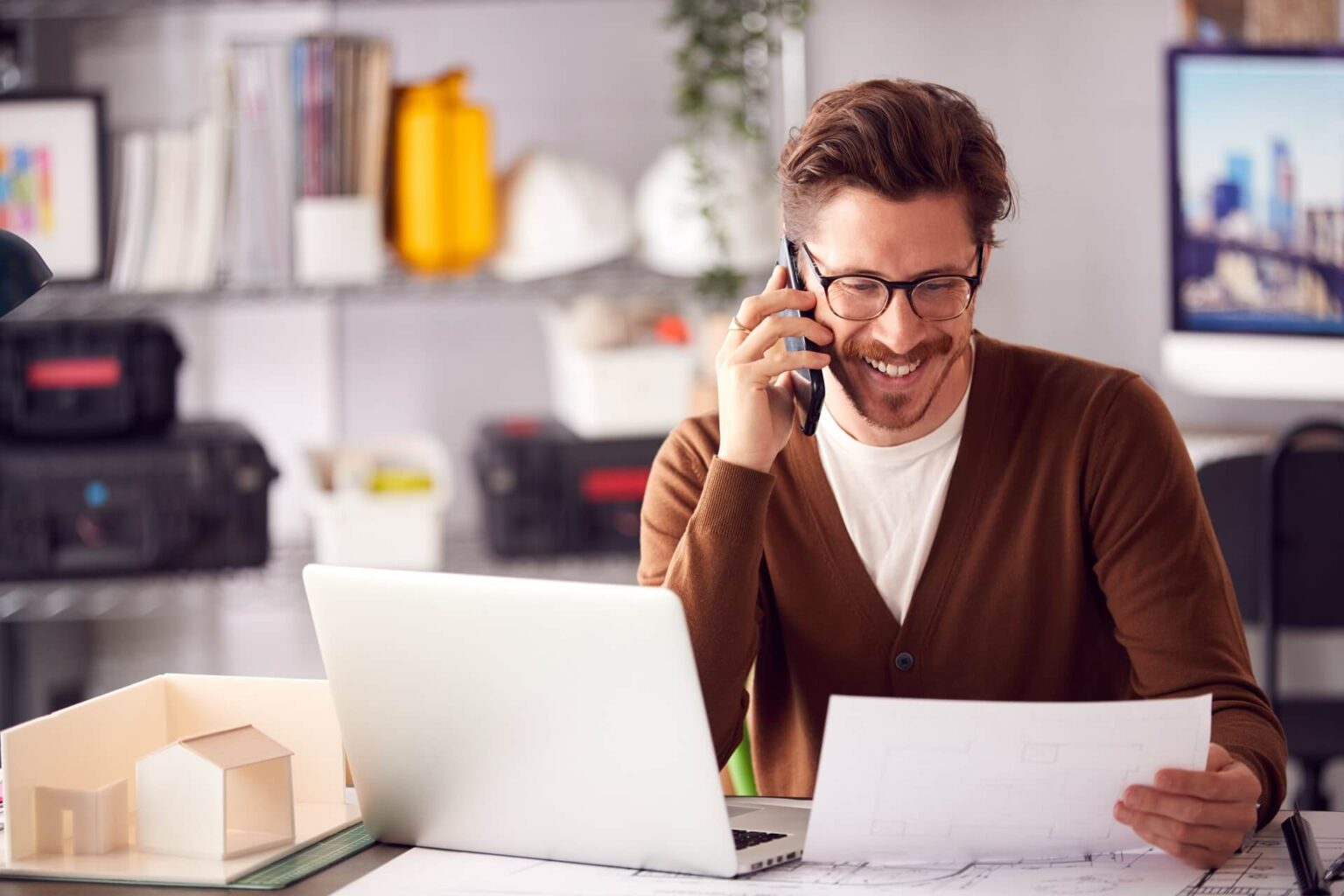 Ein Foto eines männlichen Architekten, der am Schreibtisch in seinem Büro arbeitet. Mit Laptop und Smartphone ausgestattet, verkörpert er Kreativität und Effizienz bei der Umsetzung seiner Architekturprojekte.